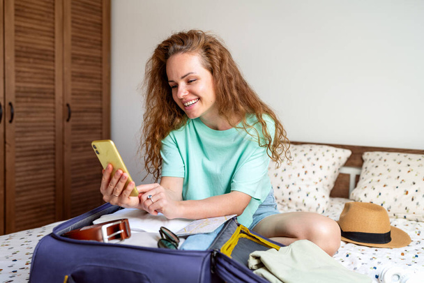 Woman checking reservation hotel and flight e-ticket in internet while packing travel bag and preparing for trip. Looking forward to traveling. - Valokuva, kuva
