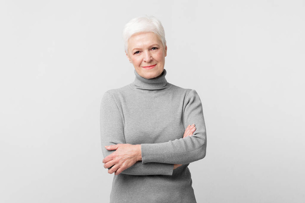 Una anciana europea se levanta con confianza con una sonrisa sobre fondo gris, perfecta para la promoción s3niorlife - Foto, Imagen