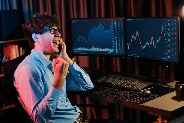 Successful business trader calling on smartphone with raising fist up of highest profit on global market online in real time at neon modern office. Concept of dynamic stock exchange growth. Gusher. - Photo, Image