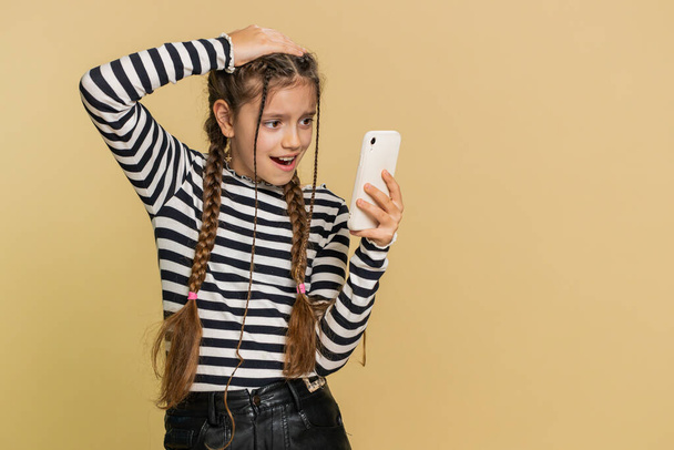 Upset sad preteen child girl kid use smartphone typing browsing, play game, loses, surprised by sudden lottery results, bad fortune, loss, fail, unlucky news. Sad children on beige background indoors - Photo, Image