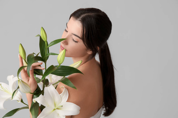 Beautiful young woman with white lily flowers on grey background, closeup - Photo, Image