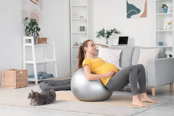 Mladá těhotná žena s fitball a kočka cvičení jóga doma - Fotografie, Obrázek