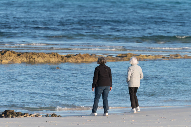 Personas mayores jubiladas relajándose en invierno en las dunas de Corralejo en la playa de arena blanca, agua azul, Fuerteventura, Islas Canarias, España en invierno - Foto, Imagen
