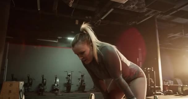 Αθλητική νεαρή γυναίκα σε activewear κλίνει με τα χέρια στα γόνατα, ενώ λαμβάνοντας διάλειμμα μετά από έντονη προπόνηση στο γυμναστήριο - Πλάνα, βίντεο