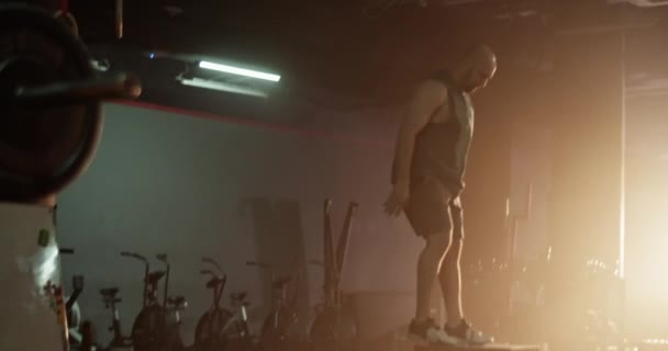 Real time tracking shot side view of strong crop male jumping from ground on to block repeatedly while training with female friend lifting heavy barbell in gym - Záběry, video