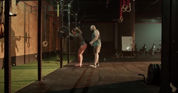 Entraîneur d'entraînement croisé menant l'entraînement personnel avec la femme musclée soulevant l'haltère pendant le cours de fitness dans la salle de gym - Séquence, vidéo