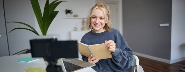 Portrait of young woman using digital camera and laptop, studying, connect to online live stream, records video for vlog, creating content, holding notebook, sitting in room. - Photo, Image