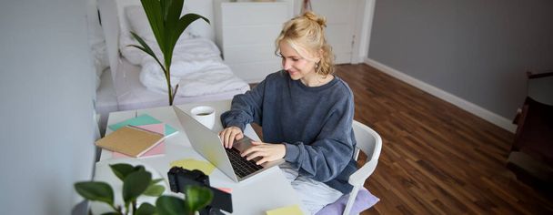 Porträt einer jungen Frau im Fernstudium, von zu Hause aus mit Laptop arbeiten, Notizen machen, Fernstudium, Online-Kurs. - Foto, Bild