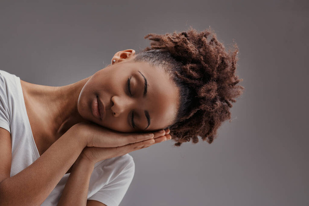Молодая женщина в спокойном сне, руки колышутся лицо, воплощает спокойствие на приглушенном фоне - Фото, изображение
