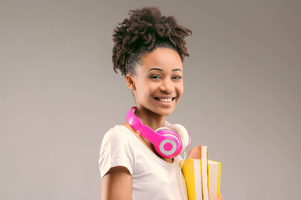 Estudiante ansioso con auriculares elegantes y un peinado afro, libros en la mano y sonrisa amplia - Foto, Imagen