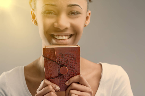 Ρίξτε μια ματιά στα μάτια μιας νεαρής γυναίκας πίσω από ένα κόκκινο, ανάγλυφο δερμάτινο ημερολόγιο. - Φωτογραφία, εικόνα