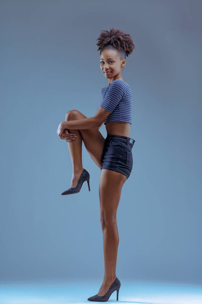 若い女性は優雅に彼女の足を持ち上げ,カジュアルなアンサンブルを補完するスタイリッシュなハイヒール - 写真・画像