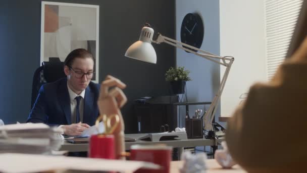 Medium over-shoulder shot of career man in suit and glasses working at desk in office, getting hit by crumpled paper from colleague, retaliating then engaging in vicious fight - Footage, Video