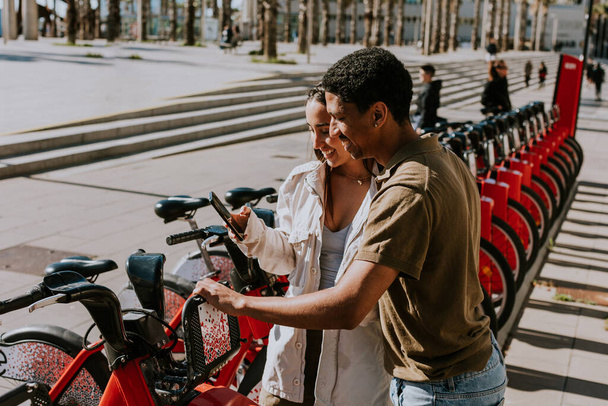 Young pair enjoying a breezy day choosing bikes from a rental station in Barcelona. - Photo, Image