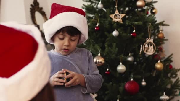 Lindo niño con sombrero rojo de Navidad y pijamas regalo de apertura en la mañana rodeado de miembros de la familia - Metraje, vídeo
