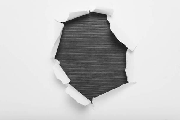 Torn hole in white paper revealing gray wood background. Space for text. - Photo, Image