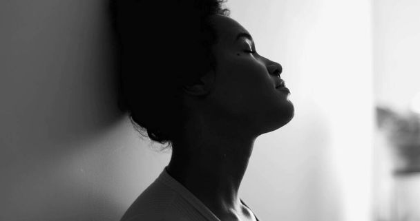 Jovem mulher afro-americana pensativa inclinada na parede, olhando para fora da janela com expressão melancólica, enfrentando a depressão em tempos difíceis iun preto e branco - Foto, Imagem