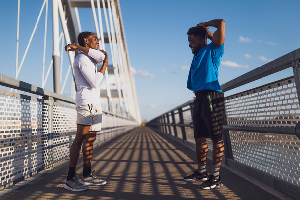 İki Afro-Amerikalı arkadaş, şehirdeki köprüde egzersiz yapıyorlar. Koşu için ısınıyorlar.. - Fotoğraf, Görsel