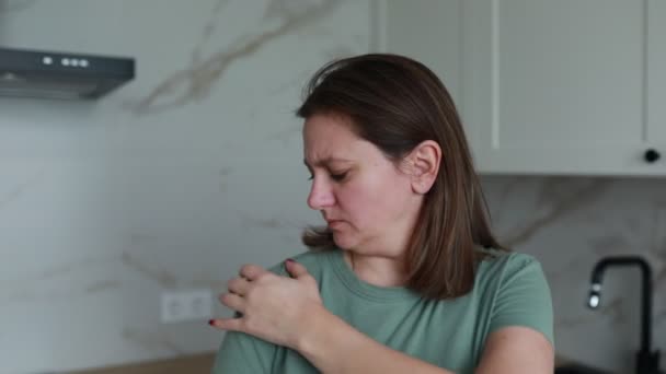 A woman in a casual green t-shirt stands in a bright, contemporary kitchen, suddenly feeling discomfort or pain. She seems to pause from her morning activities, placing her hand to her chest in a - Footage, Video
