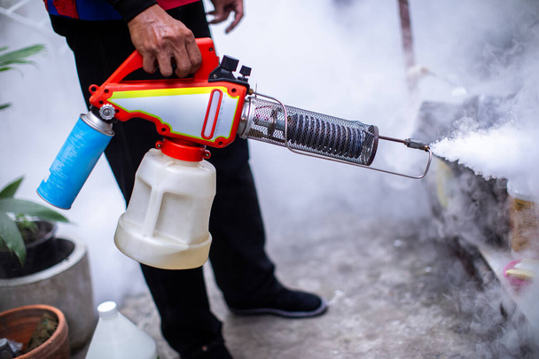Officials are spraying mosquito repellent in the area of house to prevent dengue mosquitoes as carriers of dengue fever. The officer useing fogging machine spray mosquito repellent for stop dengue. - Photo, Image