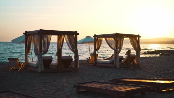 Strand cabana bedden en ligstoelen aan de kust bij zonsondergang. - Video