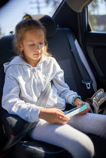Девушка сидит в машине, поглощенная своим смартфоном, с солнечным светом.. - Фото, изображение