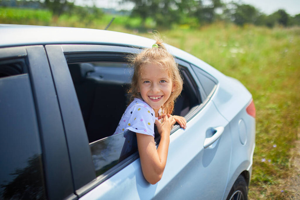 Lapsi ojentaa kätensä ulos autosta, heiluttaen kirkkaana, aurinkoisena päivänä maaseudulla.. - Valokuva, kuva