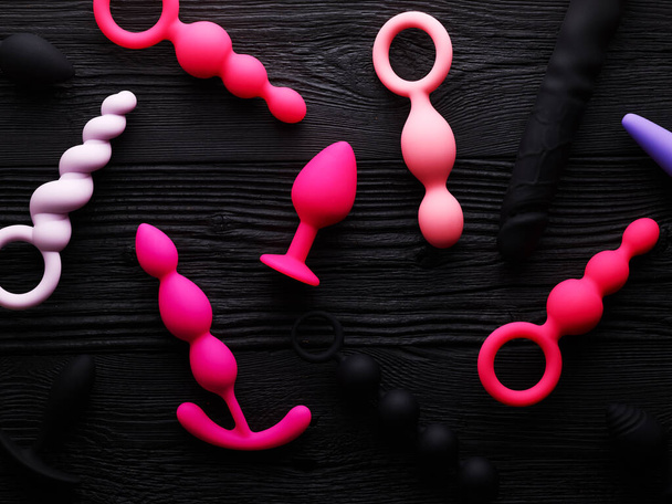 anal plugs and dildo in different shades of pink over black wooden background - Фото, зображення