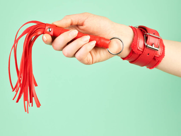 La mano de la mujer sosteniendo látigo rojo para juegos de rol para adultos sobre fondo de menta - Foto, imagen
