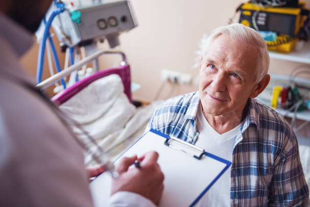 Beau vieil homme parle avec un médecin alors qu'il est assis dans la salle d'hôpital
 - Photo, image