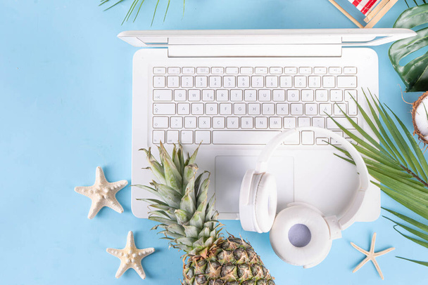 Travail et vacances. Appartement de bureau de plage d'été créatif avec ordinateur portable blanc, accessoires d'été tropicaux, feuilles de palmier, lunettes de soleil, tongs, ananas et noix de coco sur fond bleu clair - Photo, image