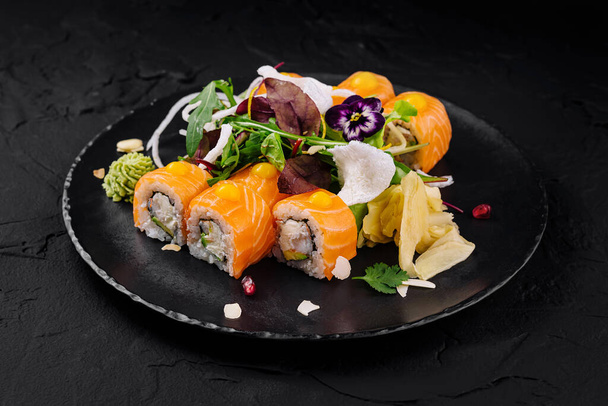 Ínyenc sushi tekercsek élénk ehető virágokkal díszítve, sötét palatáblán - Fotó, kép