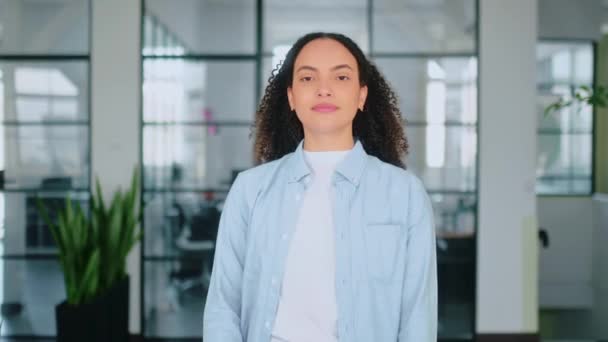 Aantrekkelijk zelfverzekerd prachtige succesvolle Spaanse of Braziliaanse jonge vrouw met krullend haar, staat in een moderne kantoorruimte met gekruiste armen, kijken en glimlachen op camera - Video