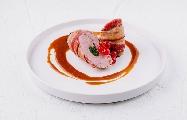 Элегантная жареная свиная вырезка с красным ягодным гарниром, подается на белой тарелке с соусом - Фото, изображение