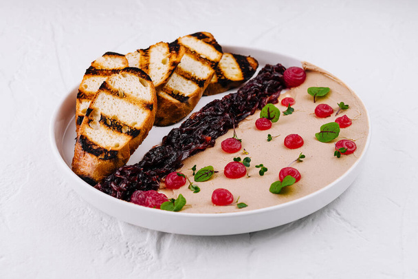 Шикарная тарелка куриного печеночного паштета, украшенная ягодным компотом, свежими травами и поджаренными ломтиками хлеба - Фото, изображение