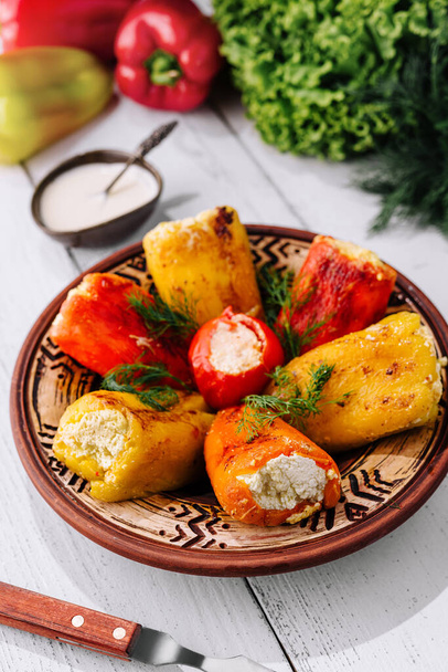 Красочные фаршированные перцы в глиняном блюде, окруженные свежими овощами и соусом - Фото, изображение