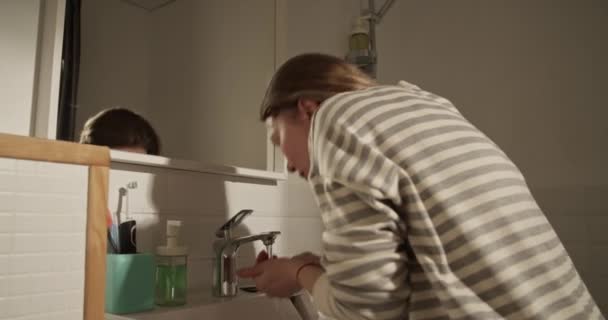 Gerçek zamanlı olarak lavabodan su toplayan ve sabah aynanın önünde durup yansımayı seyreden ve saçlara dokunan yetişkin bir kadının yan görüntüsü. - Video, Çekim