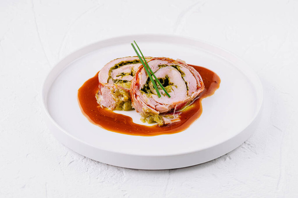 Elegante involtino di maiale ripieno di erbe aromatiche e servito con una ricca salsa marrone su un piatto bianco - Foto, immagini