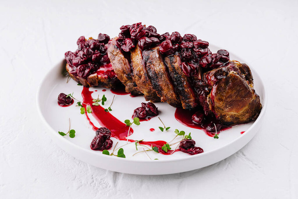 Lomo de cerdo jugoso cubierto con una rica salsa de cereza, adornado con hierbas en un plato blanco - Foto, imagen