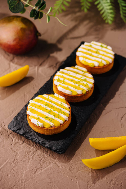Három ízletes mangós torta krémes öntettel és citromhéjjal, elegánsan tálalva palatáblán - Fotó, kép