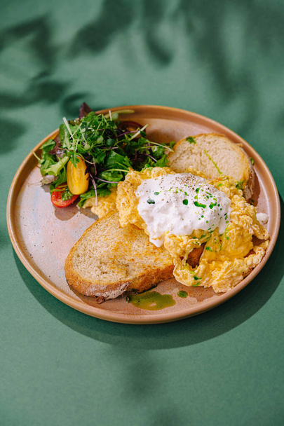 Zdravé snídaně jídlo míchaných vajec, toust, a čerstvý salát podávaný na rustikálním talíři se zeleným pozadím - Fotografie, Obrázek