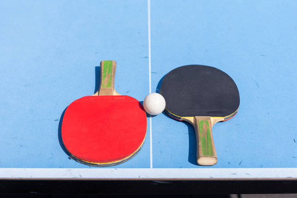 Красный и черный настольный теннис и мяч на синем столе для настольного тенниса с сеткой. Концепция пинг-понга с местом для копирования. Высокое качество фото - Фото, изображение