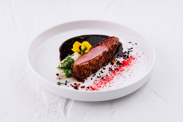 Elegante filete de res plateado con una rica salsa de vino tinto, adornado con flores comestibles sobre un fondo blanco - Foto, imagen