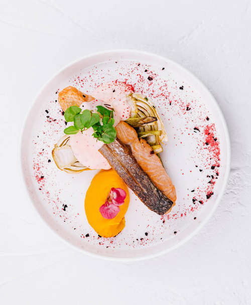 Vista dall'alto di un delizioso filetto di salmone placcato con vivaci verdure e salsa su sfondo bianco - Foto, immagini