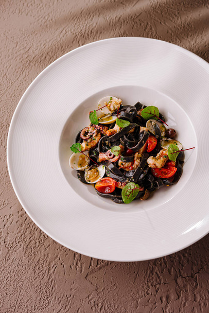 Элегантная тарелка спагетти с чернилами кальмара со смешанными морепродуктами, помидорами черри и травами - Фото, изображение
