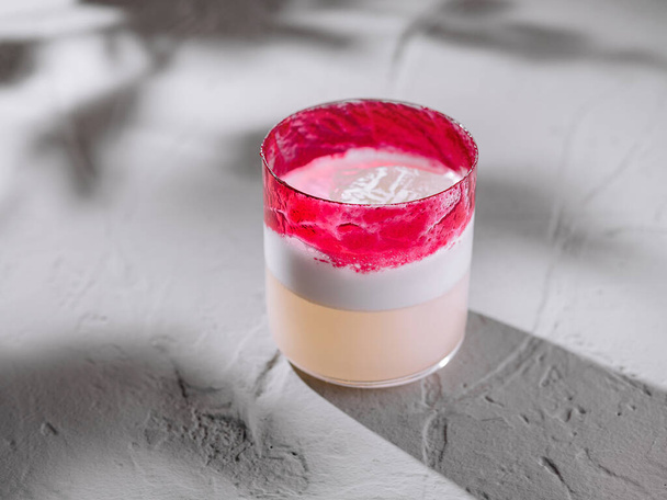 Stylový koktejl s pulzujícími růžovými a bílými vrstvami, prezentovaný na moderním, texturovaném pozadí - Fotografie, Obrázek