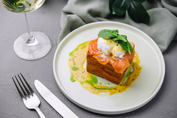 Елегантний копчений лосось на тості з яйцем, подається на білій тарілці зі склянкою білого вина - Фото, зображення