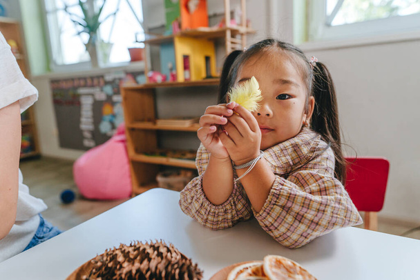 Chica jugando en la mesa con una pluma y juguetes naturales en el jardín de infantes. Enfoque selectivo. - Foto, imagen