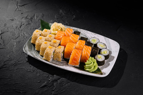 Ποικιλία από ρολά σούσι σε κεραμικό πιάτο, κομψά παρουσιάζονται σε μαύρο φόντο σχιστόλιθου - Φωτογραφία, εικόνα