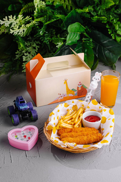 Kleurrijke kindermaaltijd met kip, friet en sap, vergezeld van een kleine speelgoedauto - Foto, afbeelding